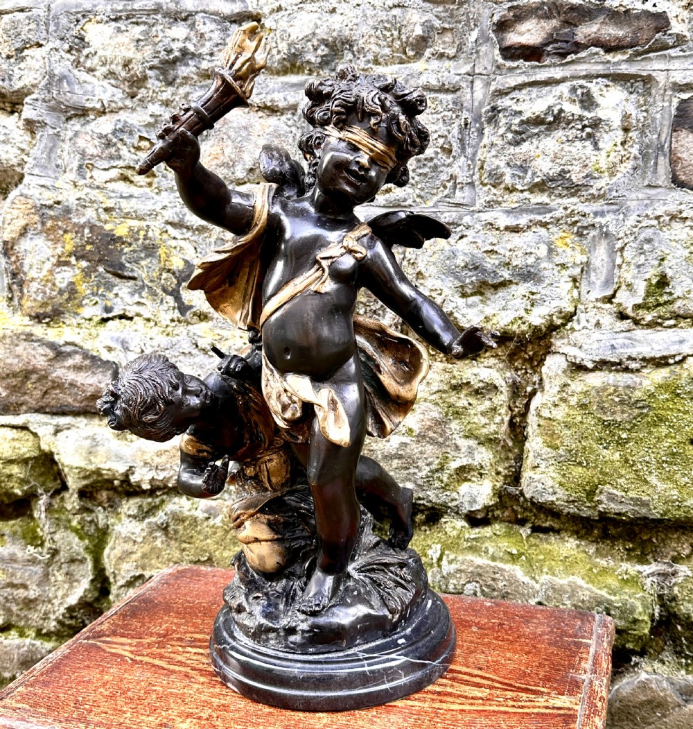 A dark bronze and parcel-gilt French sculpture depicting a blindfolded winged cherub holding a flaming torch, mounted on a round black marble base. View IV