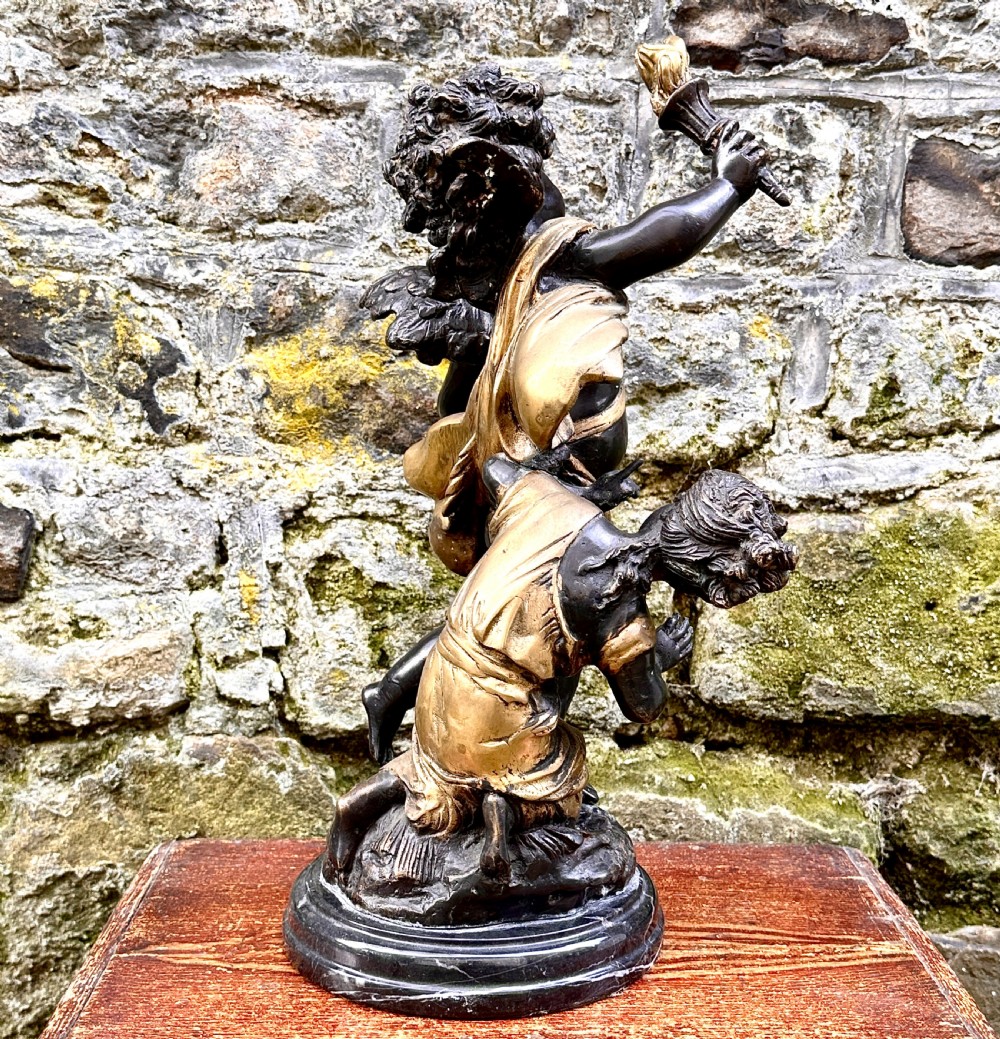 A dark bronze and parcel-gilt French sculpture depicting a blindfolded winged cherub holding a flaming torch, mounted on a round black marble base. View V