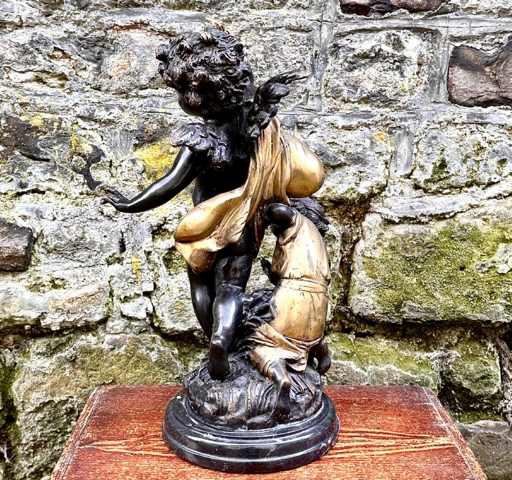 A dark bronze and parcel-gilt French sculpture depicting a blindfolded winged cherub holding a flaming torch, mounted on a round black marble base. View VI