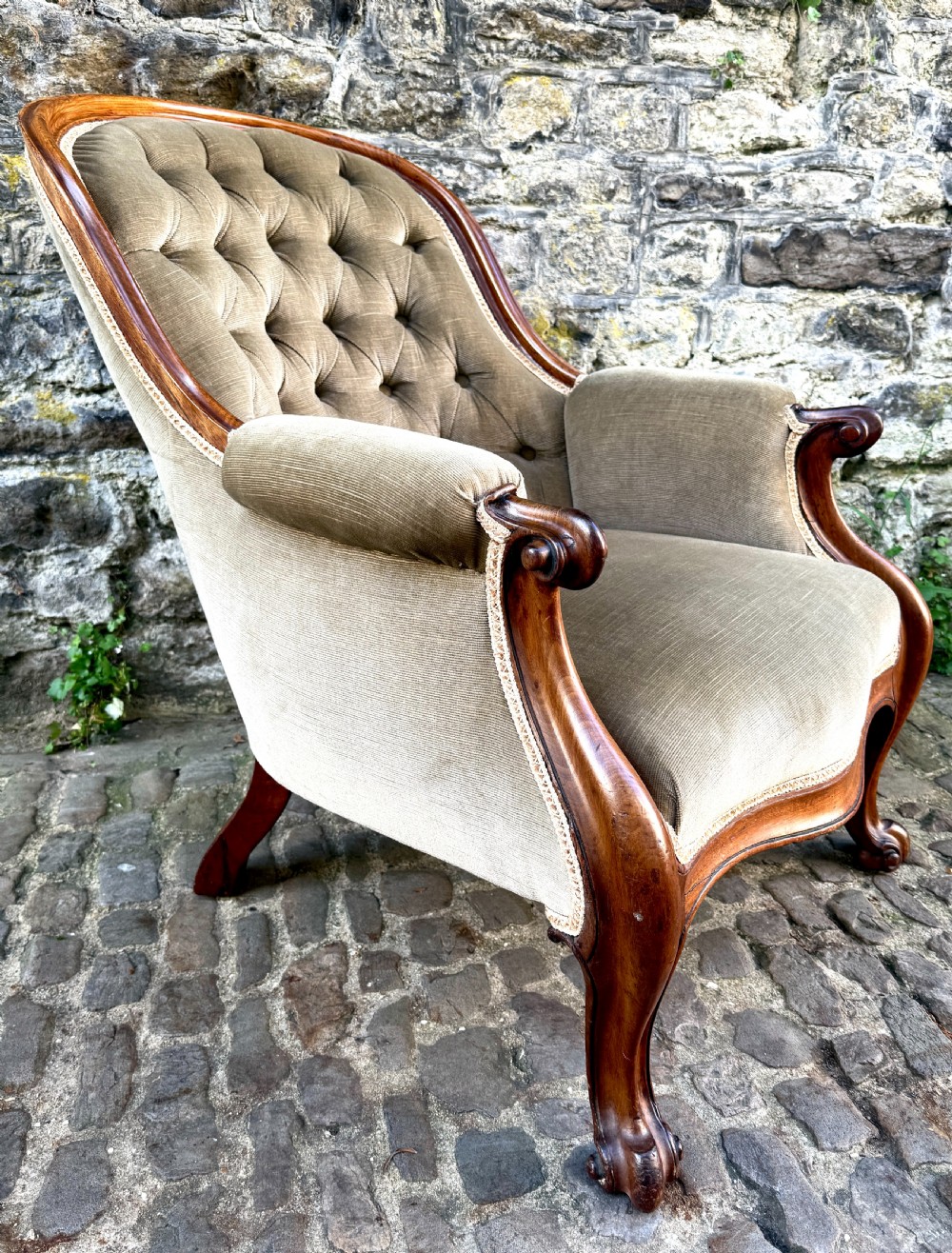 An Early Victorian walnut armchair featuring deep button-tufted olive green velvet upholstery, carved padded armrests, and cabriole front legs. View IV