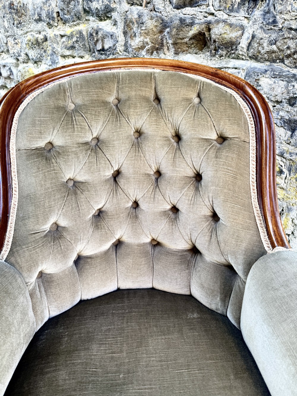 An Early Victorian walnut armchair featuring deep button-tufted olive green velvet upholstery, carved padded armrests, and cabriole front legs. View V