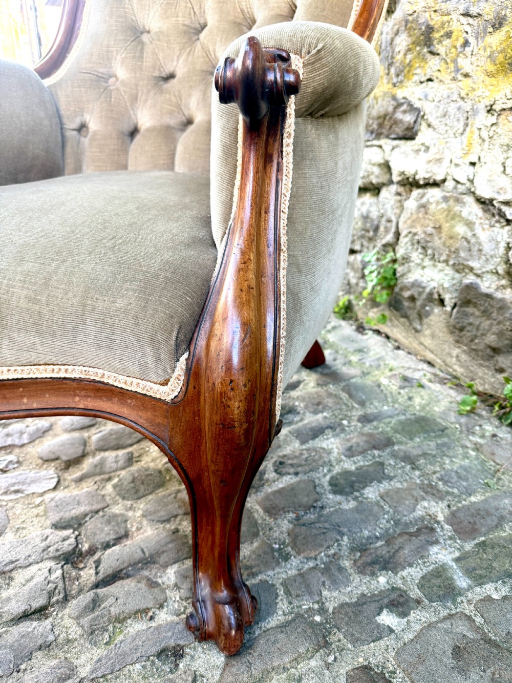 An Early Victorian walnut armchair featuring deep button-tufted olive green velvet upholstery, carved padded armrests, and cabriole front legs. View VI