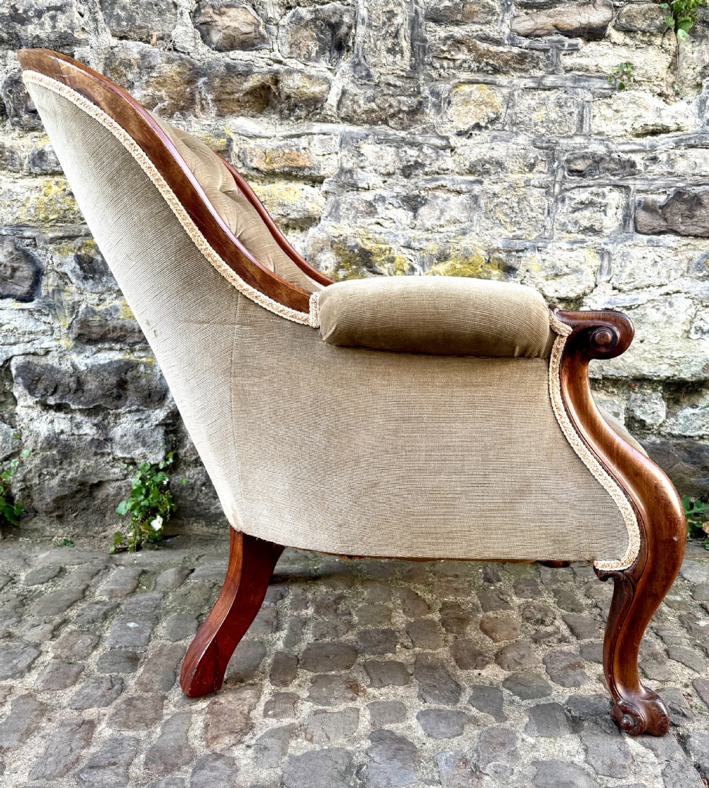 An Early Victorian walnut armchair featuring deep button-tufted olive green velvet upholstery, carved padded armrests, and cabriole front legs. View VIII