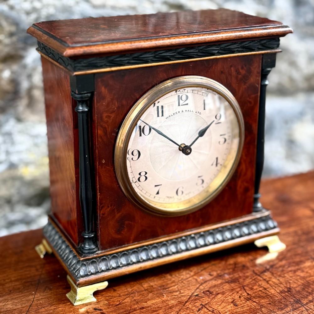 An early 20th-century rectangular mahogany and burr walnut mantel clock featuring ebonised side columns, a white circular dial signed Walker & Hall Ltd., and brass bracket feet. View IV