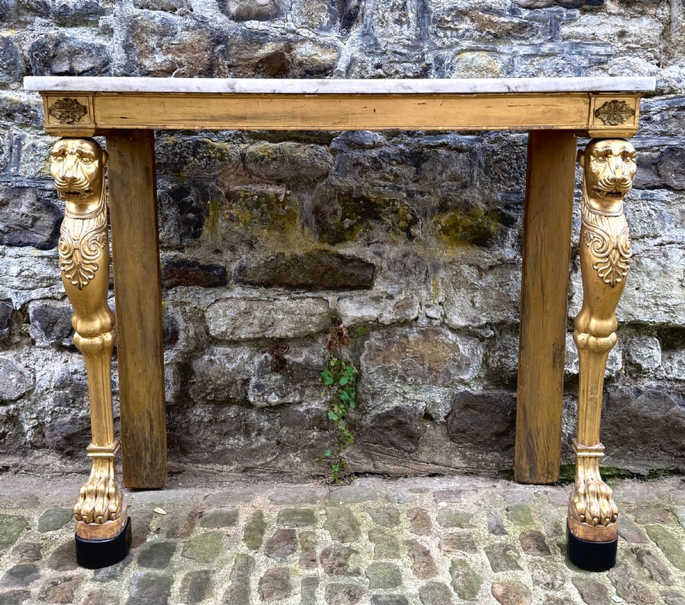 A Regency giltwood console table featuring a grey marble top supported by two carved lion monopodia front legs.