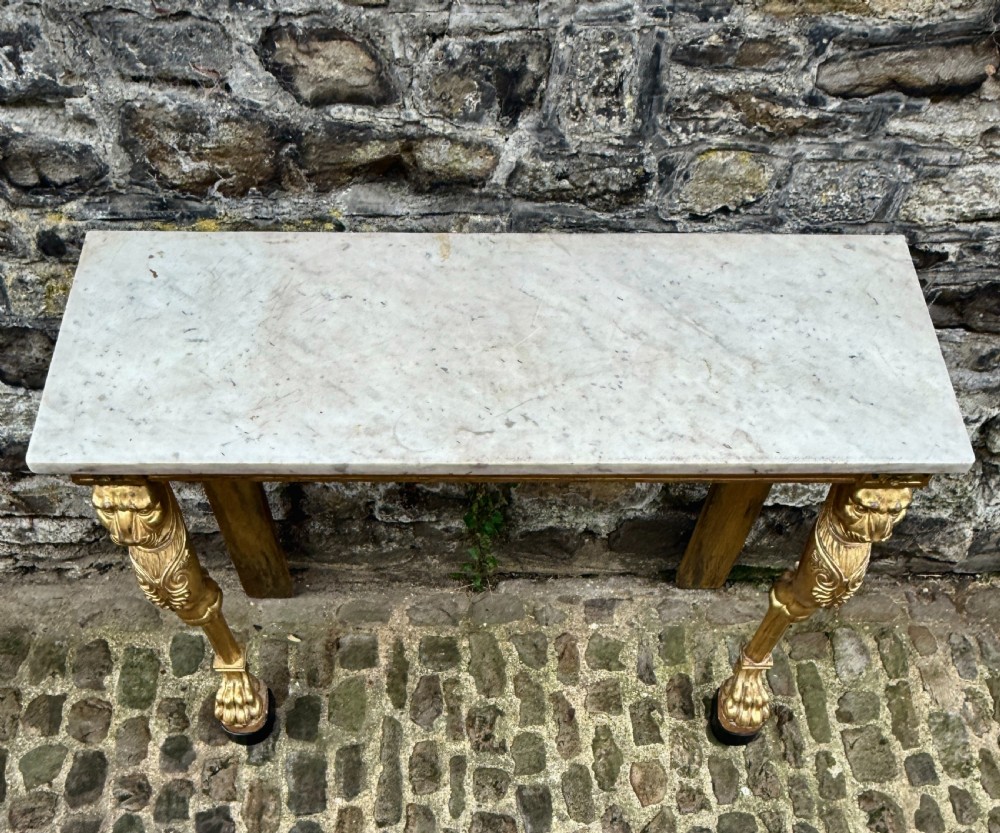 A Regency giltwood console table featuring a grey marble top supported by two carved lion monopodia front legs. View VII