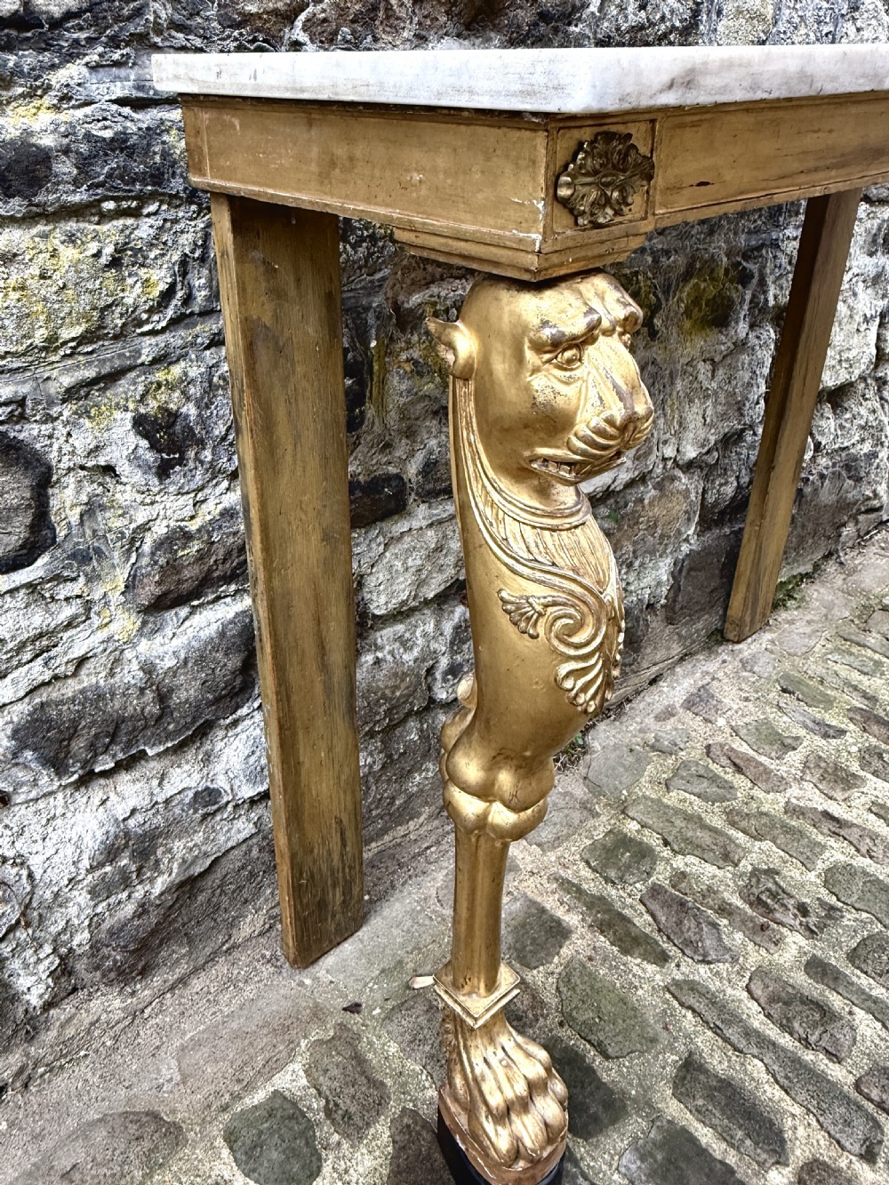 A Regency giltwood console table featuring a grey marble top supported by two carved lion monopodia front legs. View IX