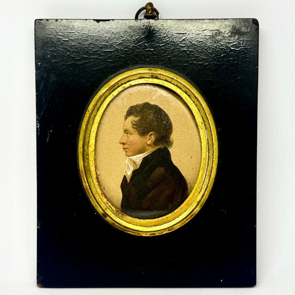 A Regency profile portrait miniature of a gentleman in a white cravat, set within an oval gilt bezel and rectangular black ebonised frame.
