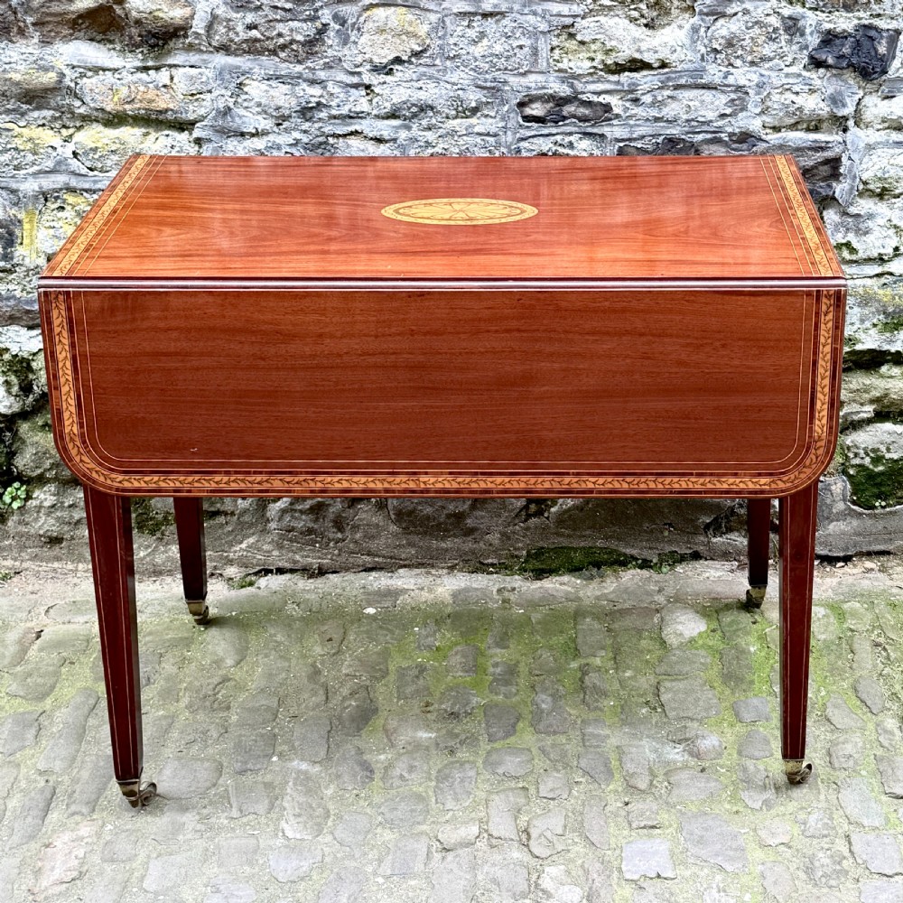 A George III mahogany Pembroke table with satinwood inlay, tapered square legs, and brass castors. View II