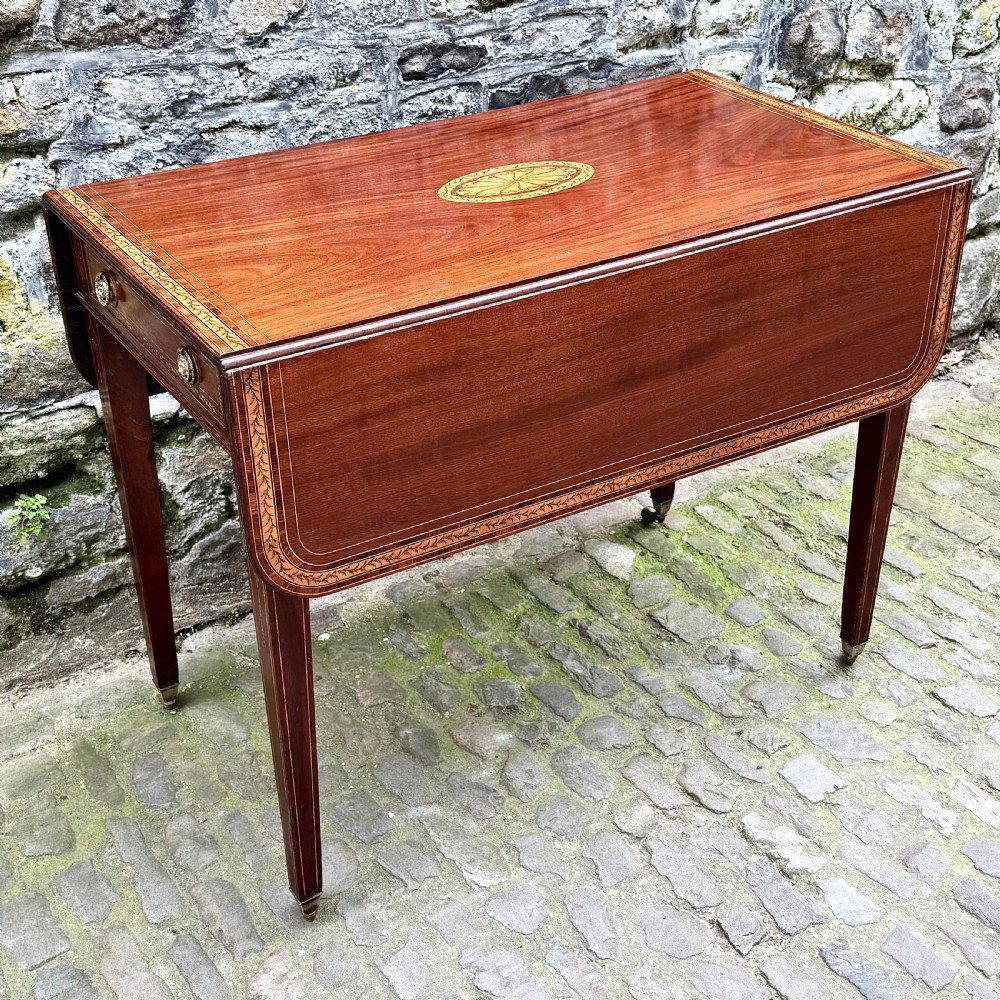 A George III mahogany Pembroke table with satinwood inlay, tapered square legs, and brass castors. View IV