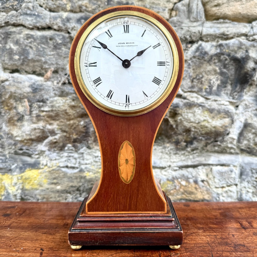 An Edwardian mahogany balloon-shaped mantel clock featuring a circular dial with Roman numerals and central marquetry inlay on a stepped base.
