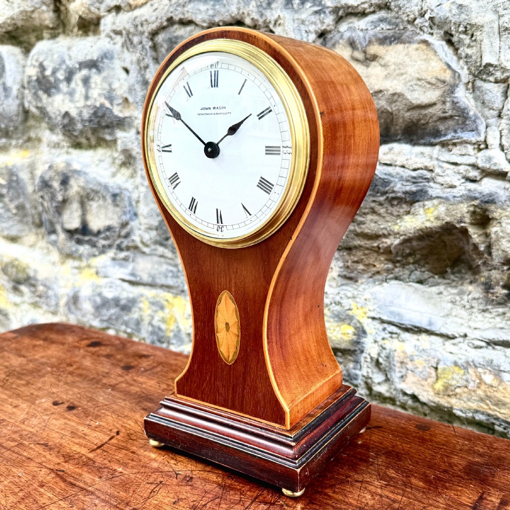 An Edwardian mahogany balloon-shaped mantel clock featuring a circular dial with Roman numerals and central marquetry inlay on a stepped base. View II