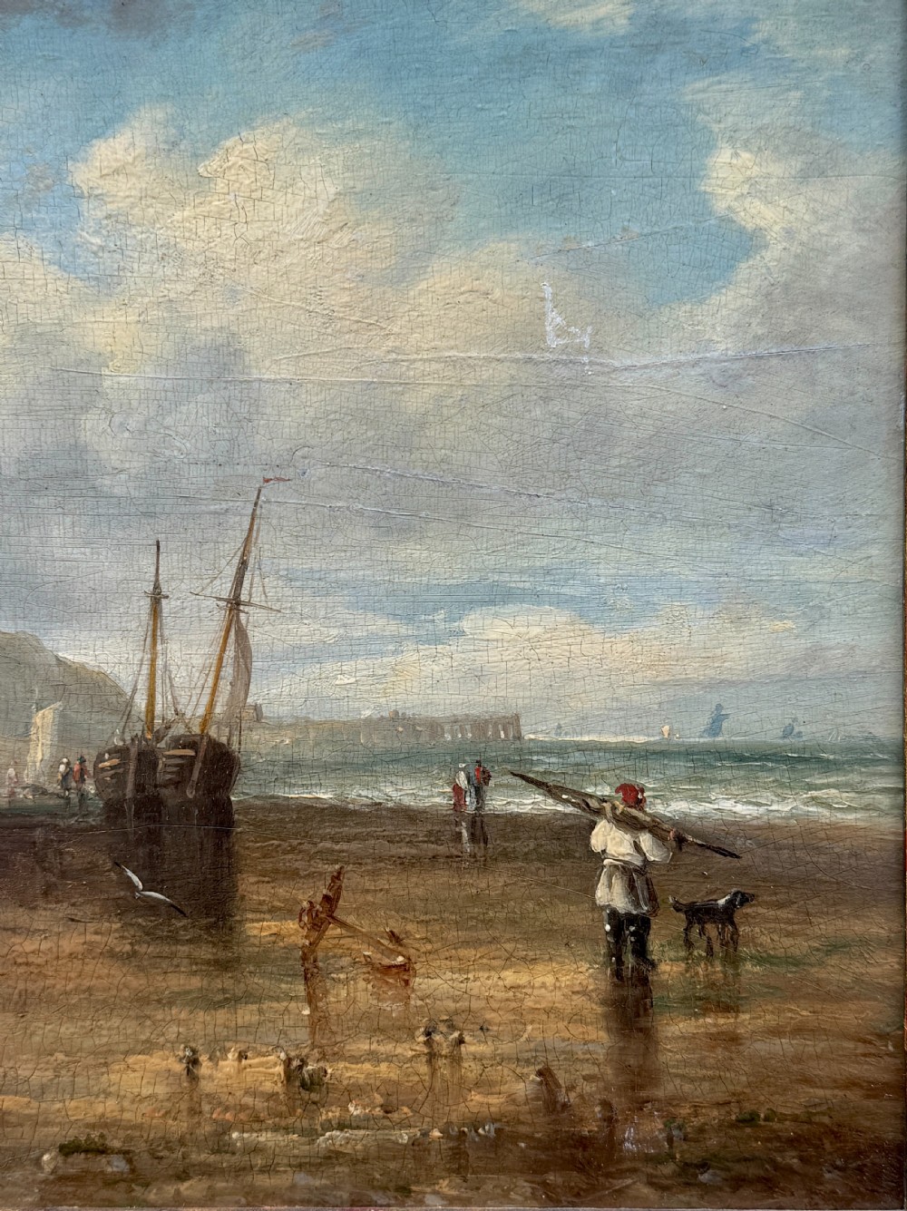 A 19th-century oil painting depicting a coastal seascape with figures, horses, and boats on a shoreline below cliffs, set within a wide timber frame with a gilded inner slip. View IV