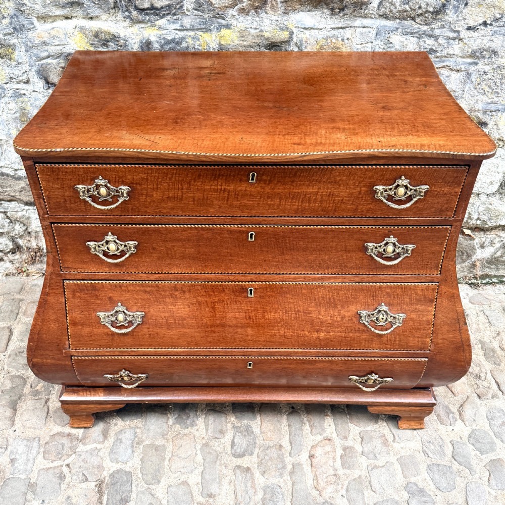 A late 18th-century Dutch mahogany chest of drawers featuring a shaped bombee profile, four long drawers with decorative brass handles, and bracket feet. View II