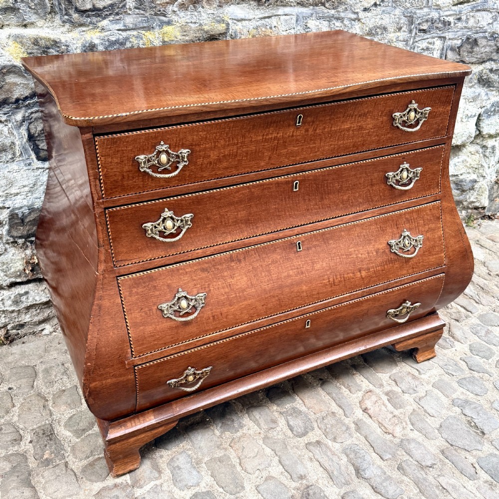 A late 18th-century Dutch mahogany chest of drawers featuring a shaped bombee profile, four long drawers with decorative brass handles, and bracket feet. View IV