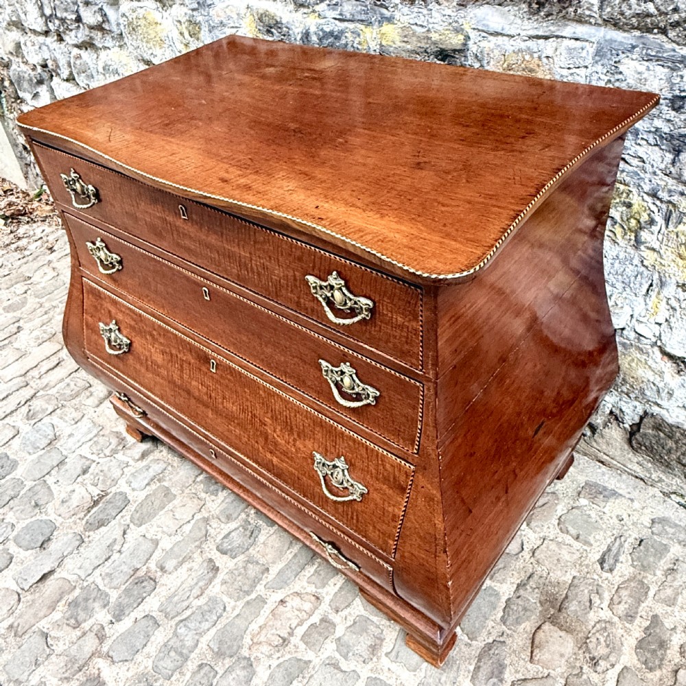 A late 18th-century Dutch mahogany chest of drawers featuring a shaped bombee profile, four long drawers with decorative brass handles, and bracket feet. View VI