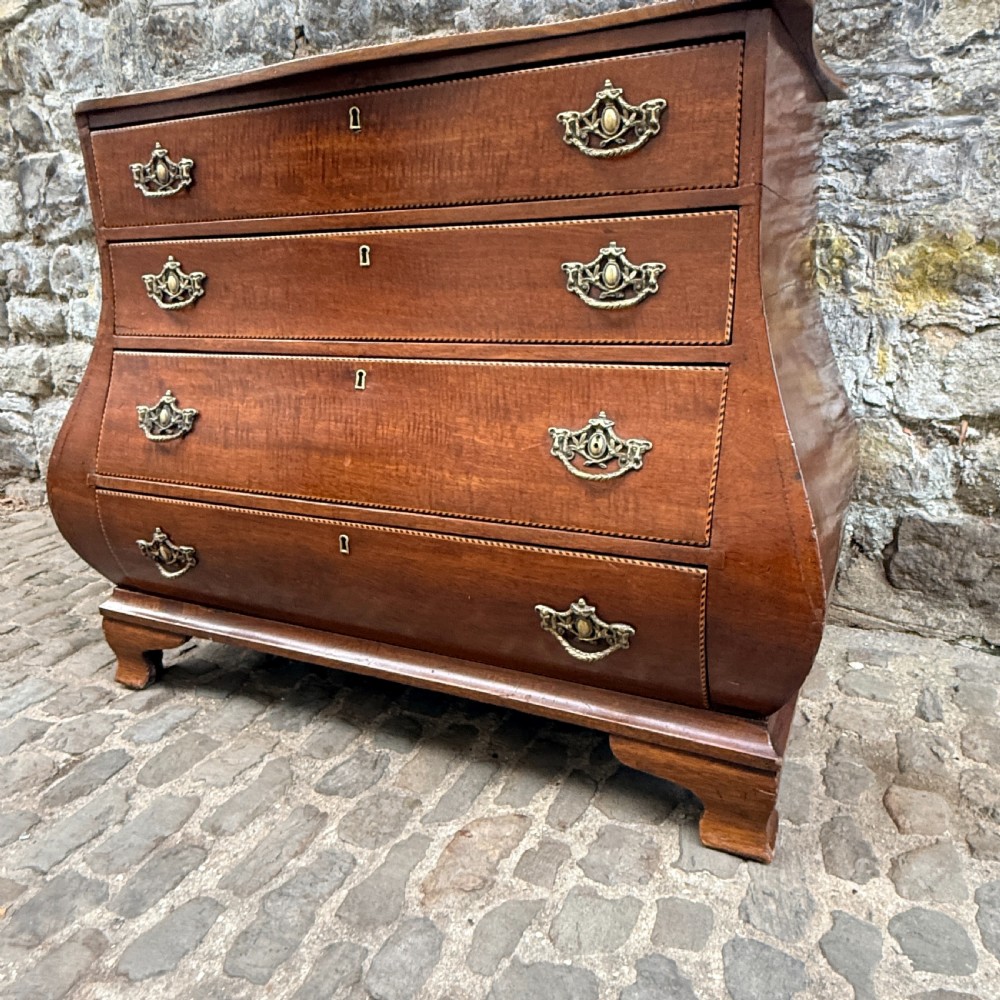 A late 18th-century Dutch mahogany chest of drawers featuring a shaped bombee profile, four long drawers with decorative brass handles, and bracket feet. View VII