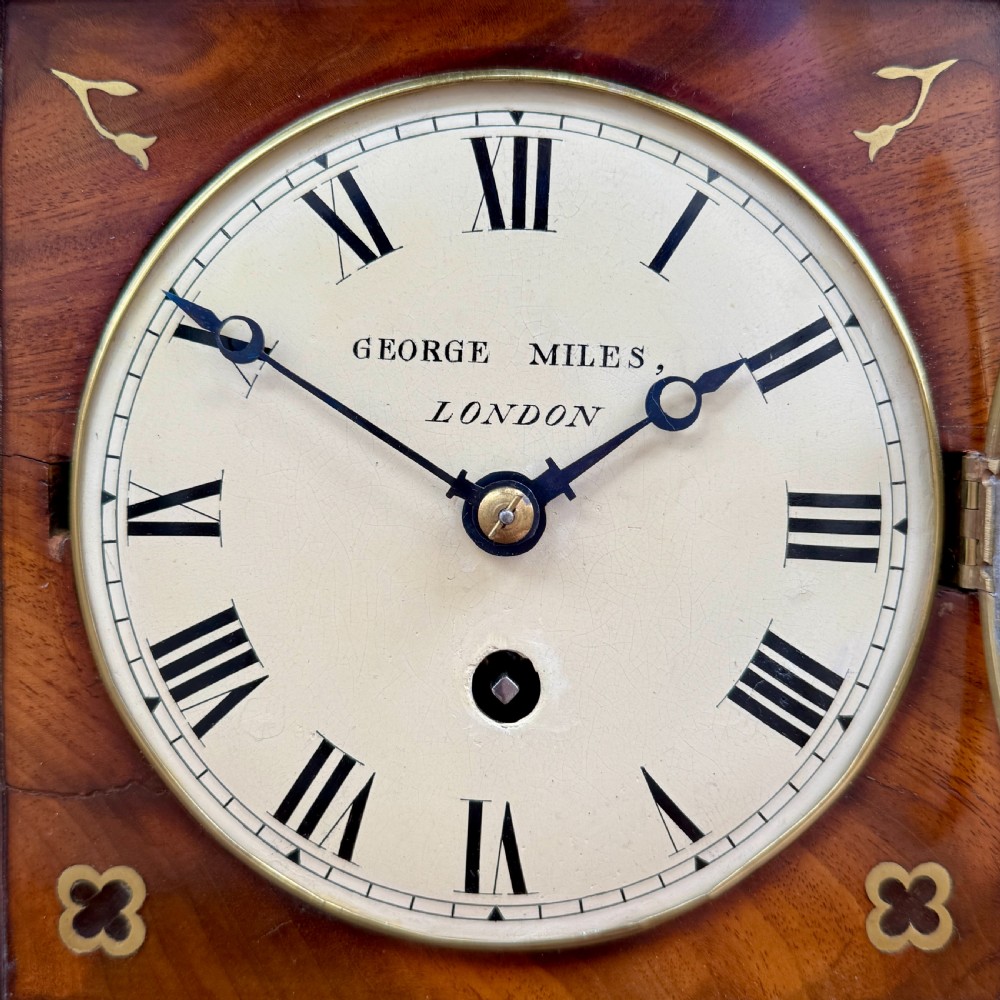 A Regency mahogany library clock featuring brass floral inlay, a pineapple finial, brass ball feet, and a white dial signed George Miles London. View IV