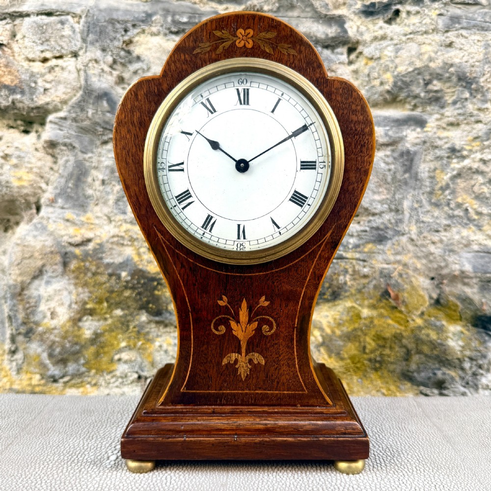 An Art Nouveau inlaid mahogany mantel clock featuring foliate marquetry, a white enamel dial with Roman numerals, and brass bun feet.