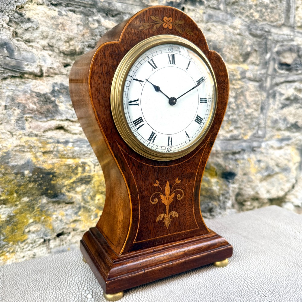 An Art Nouveau inlaid mahogany mantel clock featuring foliate marquetry, a white enamel dial with Roman numerals, and brass bun feet. View III