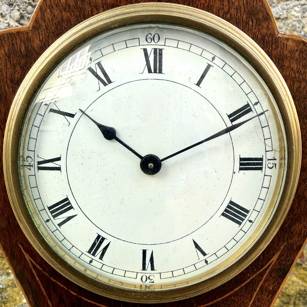 An Art Nouveau inlaid mahogany mantel clock featuring foliate marquetry, a white enamel dial with Roman numerals, and brass bun feet. View IV