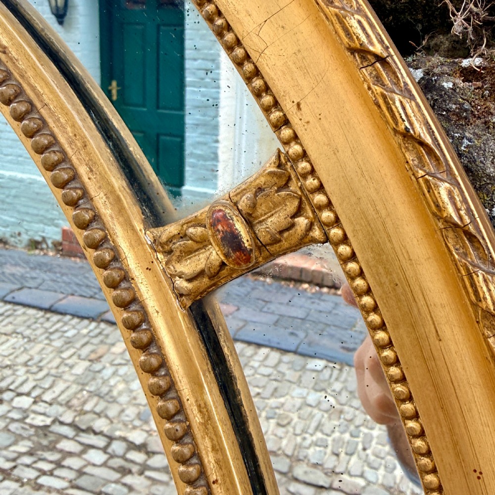 An oval giltwood wall mirror featuring a double-ring frame connected by small decorative spacers and decorated with beaded moulding. View III