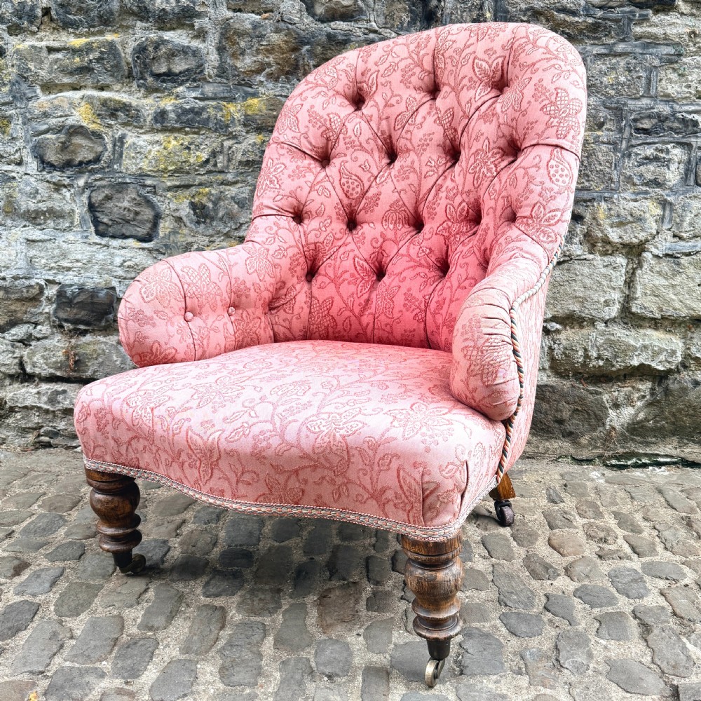 A mid-19th century French low bedroom chair featuring pink patterned button-tufted upholstery and turned wooden front legs on castors. View II