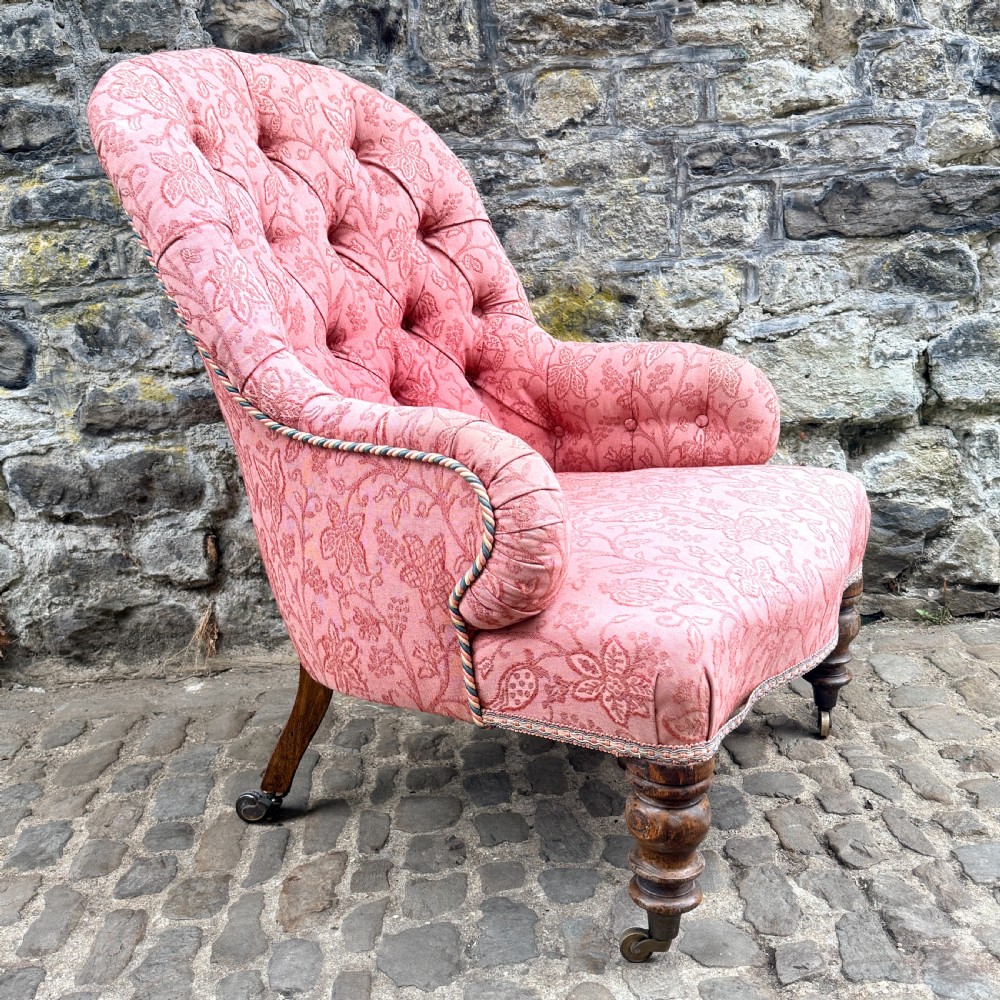 A mid-19th century French low bedroom chair featuring pink patterned button-tufted upholstery and turned wooden front legs on castors. View III