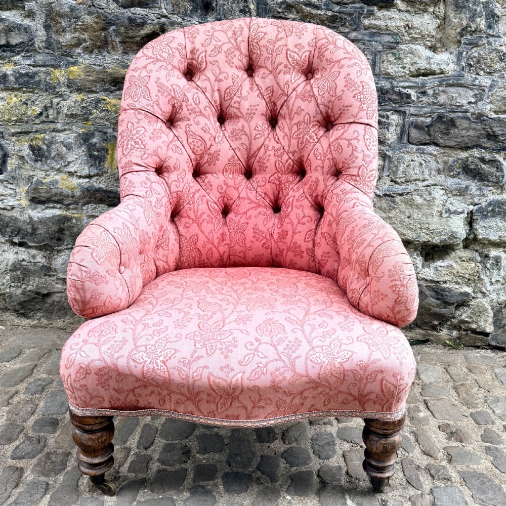A mid-19th century French low bedroom chair featuring pink patterned button-tufted upholstery and turned wooden front legs on castors. View VI