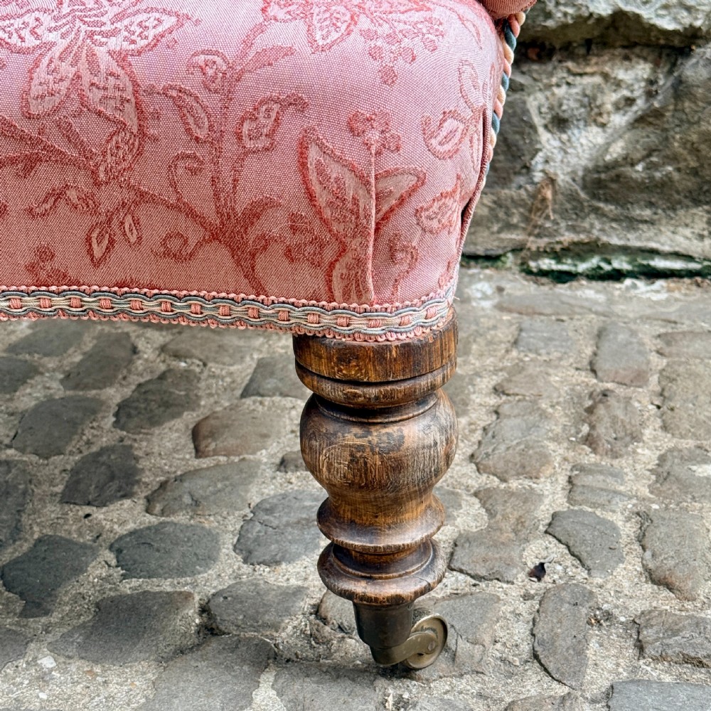 A mid-19th century French low bedroom chair featuring pink patterned button-tufted upholstery and turned wooden front legs on castors. View VII