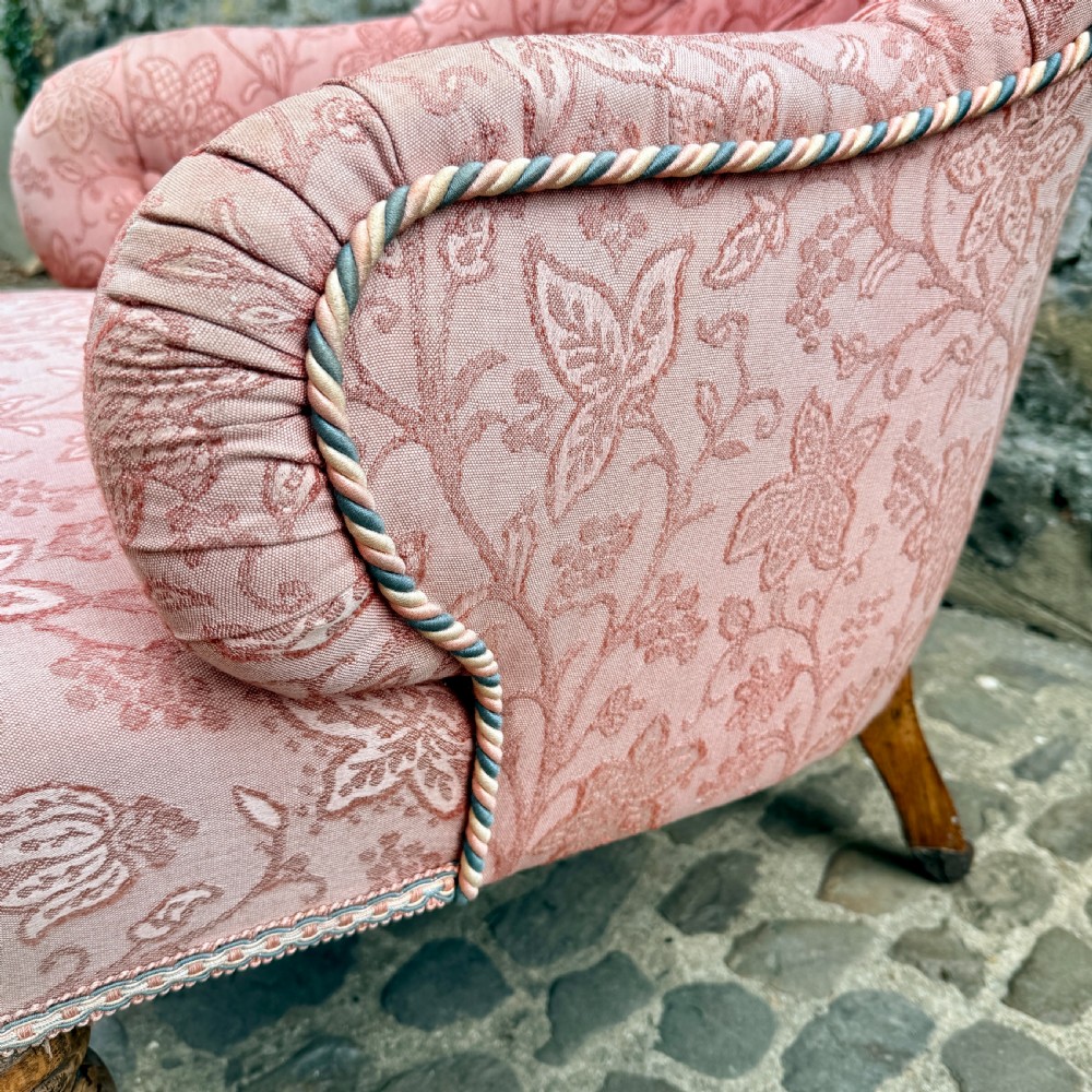 A mid-19th century French low bedroom chair featuring pink patterned button-tufted upholstery and turned wooden front legs on castors. View VIII