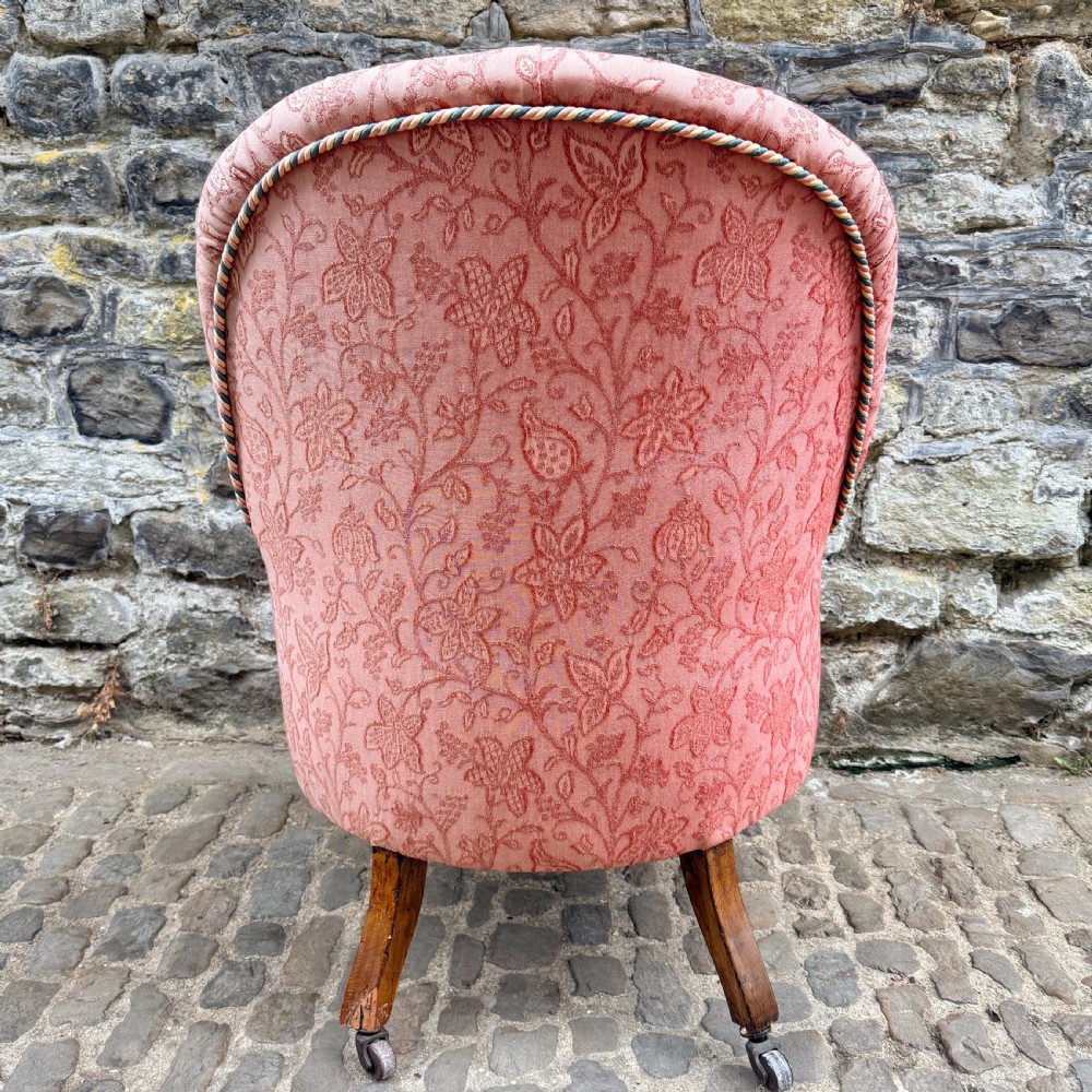 A mid-19th century French low bedroom chair featuring pink patterned button-tufted upholstery and turned wooden front legs on castors. View IX