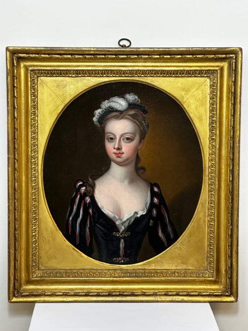 fig 1. An 18th-century oil portrait of a lady in a black bodice and feathered headpiece within an oval spandrel inside a square gilded frame.