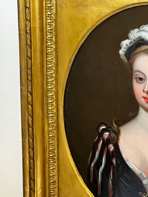 fig 2. An 18th-century oil portrait of a lady in a black bodice and feathered headpiece within an oval spandrel inside a square gilded frame.