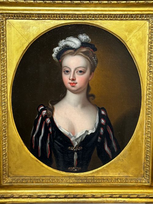 fig 6. An 18th-century oil portrait of a lady in a black bodice and feathered headpiece within an oval spandrel inside a square gilded frame.