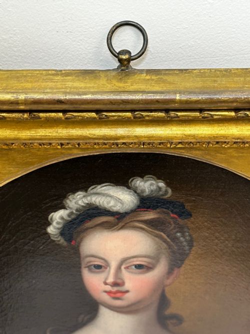 fig 8. An 18th-century oil portrait of a lady in a black bodice and feathered headpiece within an oval spandrel inside a square gilded frame.