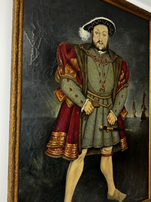 fig 2. A large oil painting in a gilded frame depicting King Henry VIII standing in Tudor costume with jewels, dagger, and feathered cap against a dark backdrop.