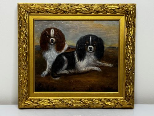 fig 1. A nineteenth-century oil painting depicting two King Charles Spaniels resting outdoors, enclosed within an ornate gilded frame decorated with carved laurel leaves.