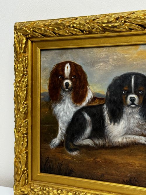 fig 2. A nineteenth-century oil painting depicting two King Charles Spaniels resting outdoors, enclosed within an ornate gilded frame decorated with carved laurel leaves.