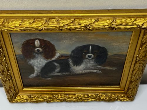 fig 3. A nineteenth-century oil painting depicting two King Charles Spaniels resting outdoors, enclosed within an ornate gilded frame decorated with carved laurel leaves.