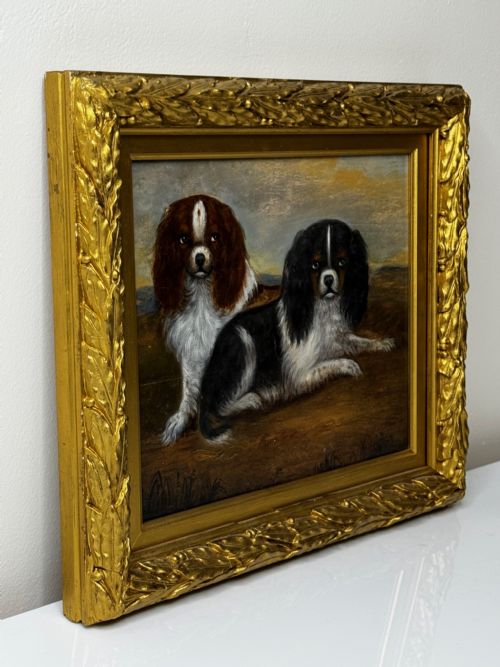 fig 4. A nineteenth-century oil painting depicting two King Charles Spaniels resting outdoors, enclosed within an ornate gilded frame decorated with carved laurel leaves.