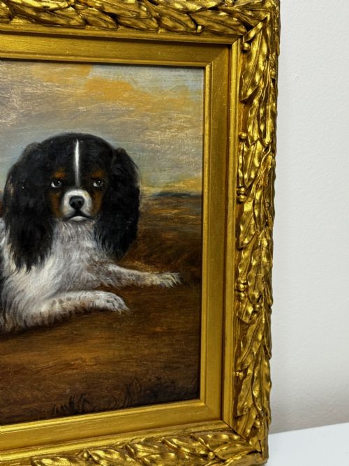 fig 5. A nineteenth-century oil painting depicting two King Charles Spaniels resting outdoors, enclosed within an ornate gilded frame decorated with carved laurel leaves.