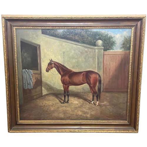 fig 1. A framed oil painting depicting a bay racehorse standing in a stable yard, housed in a moulded dark wood and gilt frame.