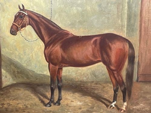 fig 7. A framed oil painting depicting a bay racehorse standing in a stable yard, housed in a moulded dark wood and gilt frame.