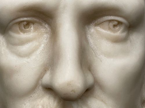 fig 2. A carved off-white marble bust depicting a bald male figure with a prominent moustache wearing classical draped fabric across the shoulders.