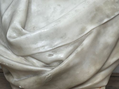 fig 7. A carved off-white marble bust depicting a bald male figure with a prominent moustache wearing classical draped fabric across the shoulders.