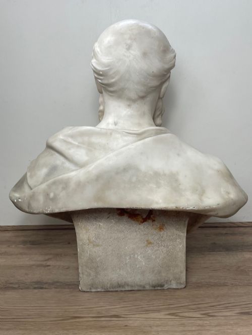 fig 11. A carved off-white marble bust depicting a bald male figure with a prominent moustache wearing classical draped fabric across the shoulders.