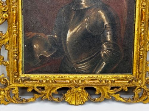 fig 6. An antique profile portrait painting of a man wearing full steel armour, set within an ornate gilded frame decorated with carved shell and scroll motifs.