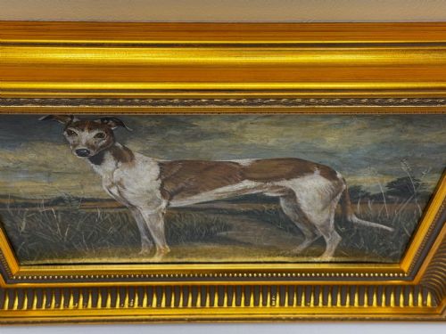 fig 2. An antique Edwardian oil painting depicting a tan and white lurcher dog in a landscape, set within an ornate gilded frame.