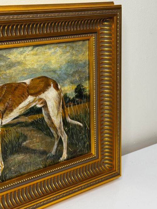 fig 4. An antique Edwardian oil painting depicting a tan and white lurcher dog in a landscape, set within an ornate gilded frame.